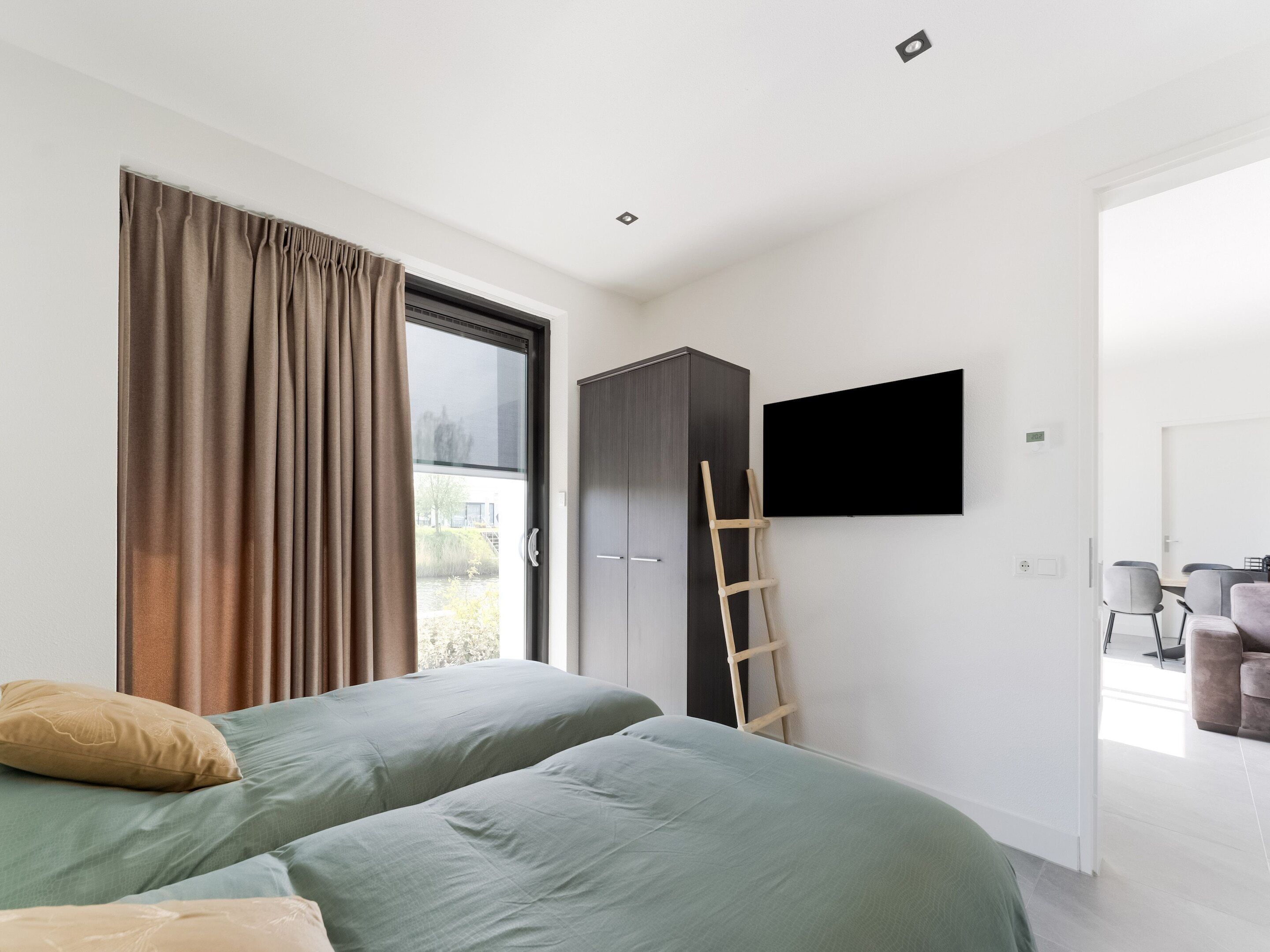 A modern bedroom with two beds, a wardrobe, a TV, and a view of the outdoors.