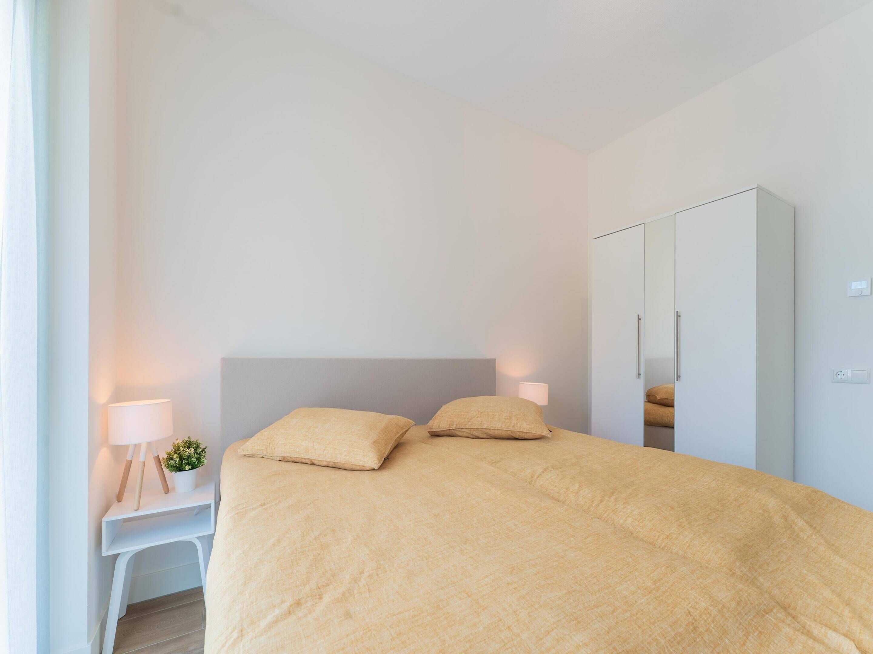 A bedroom with a bed, bedside lamps, a small table with a plant, and a wardrobe.