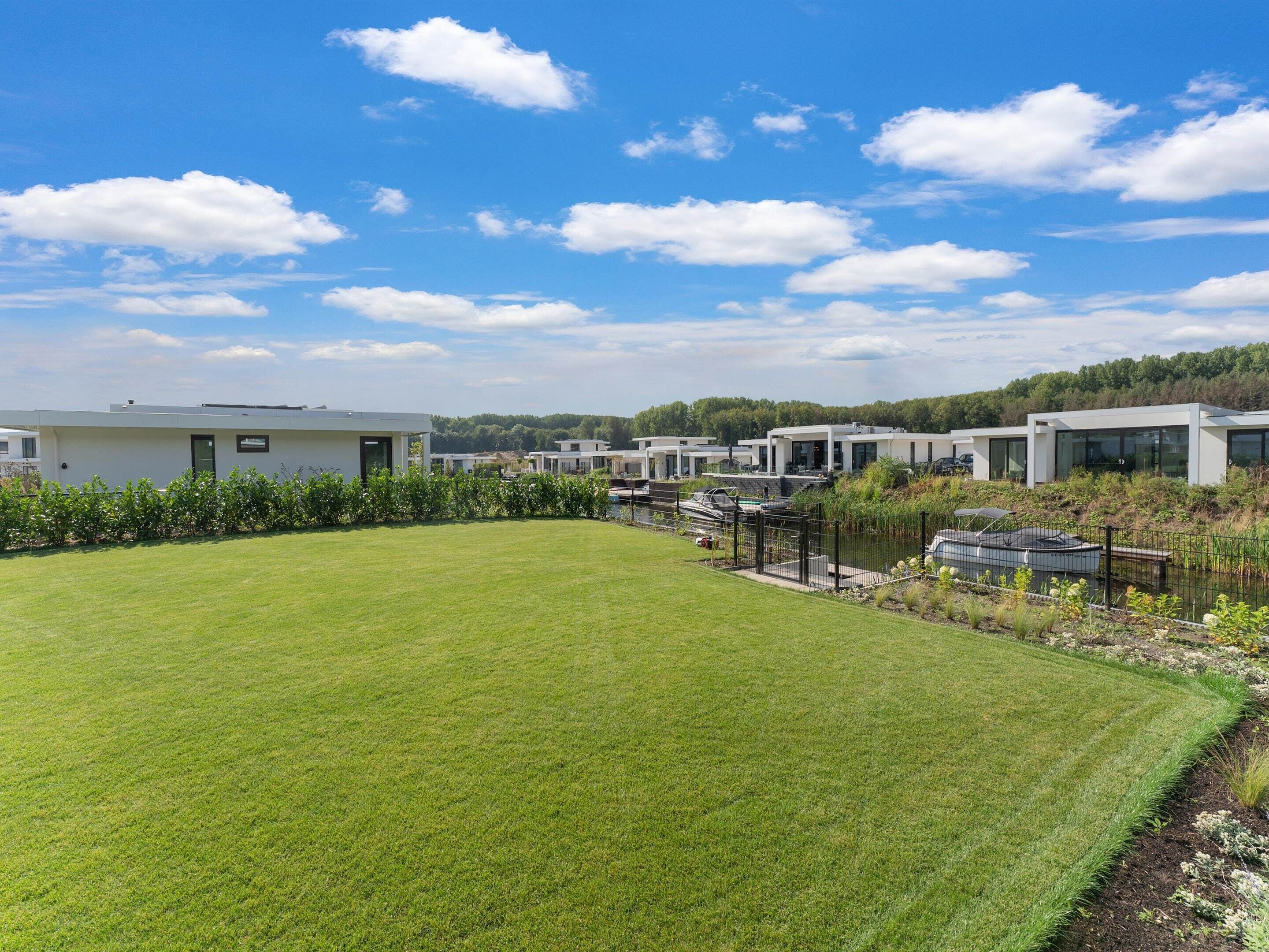 A modern residential area with multiple houses, a well-maintained lawn, and a body of water with boats.