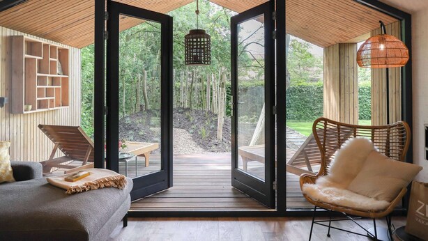 A modern interior with a large sliding glass door leading to an outdoor deck, wooden furniture, and a hanging light fixture. - Cosy Holiday Home With Private Sauna (Wissenkerke)