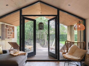 A modern interior with a large sliding glass door leading to an outdoor deck, wooden furniture, and a hanging light fixture. - Cosy Holiday Home With Private Sauna (Wissenkerke)