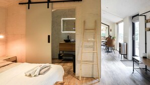 A modern bedroom with a wooden bed, a bedside table, a nightstand, a wooden ladder, and a bathroom with a mirror, sink, and towel rack. - Cosy Holiday Home With Private Sauna (Wissenkerke)