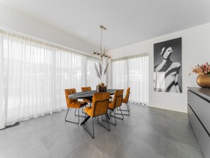 A modern dining area with a round table, orange chairs, and a chandelier. - Villa in Zeewolde for 6 Person (Zeewolde)