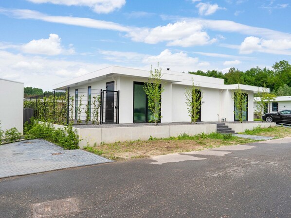 A modern two-story house with a flat roof, large windows, and a paved driveway.