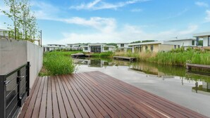 Une propriété moderne située au bord de l’eau, dotée d’une terrasse en bois, d’un canal et de maisons au style contemporain.