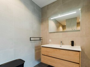 A modern bathroom with a large mirror, a white sink, and a wooden vanity.