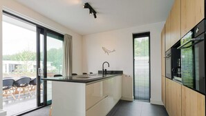 Une cuisine moderne dotée d’un îlot central, d’un coin repas avec des chaises et d’une vue dégagée grâce à une porte vitrée.