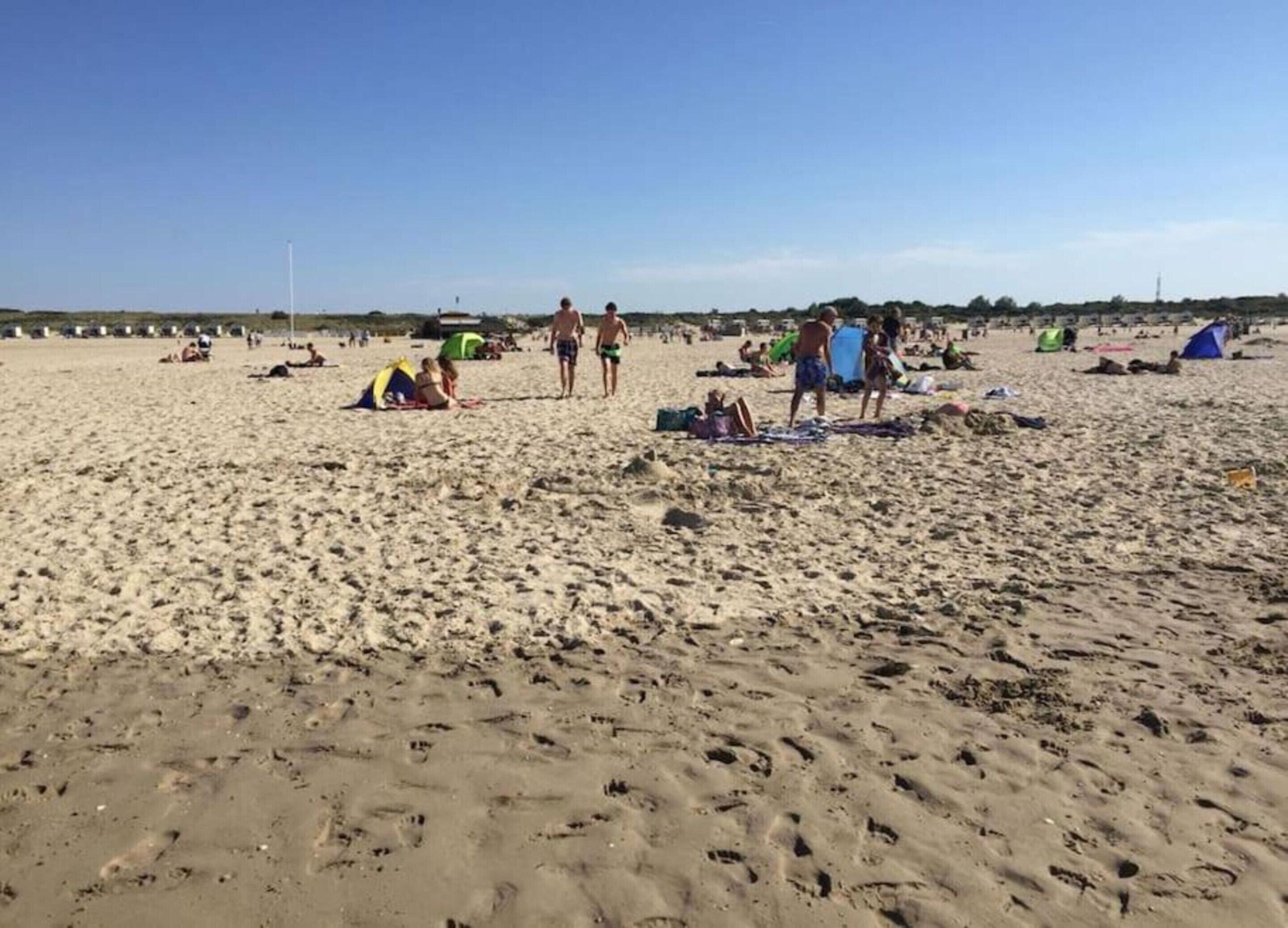 A sandy beach with footprints, tents, and people.
