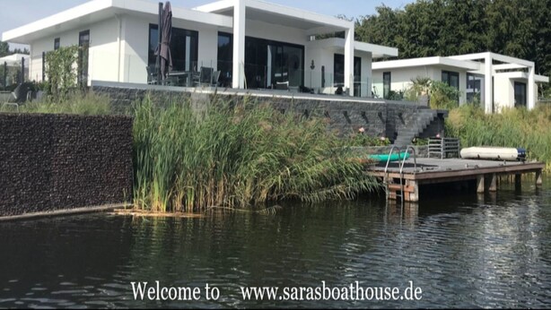 A modern house with a large glass facade, a dock, and a pond. - Exclusive Villa With Boat Terrace (Zeewolde)