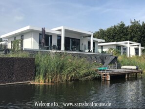 A modern house with a large glass facade, a dock, and a pond. - Exclusive Villa With Boat Terrace (Zeewolde)