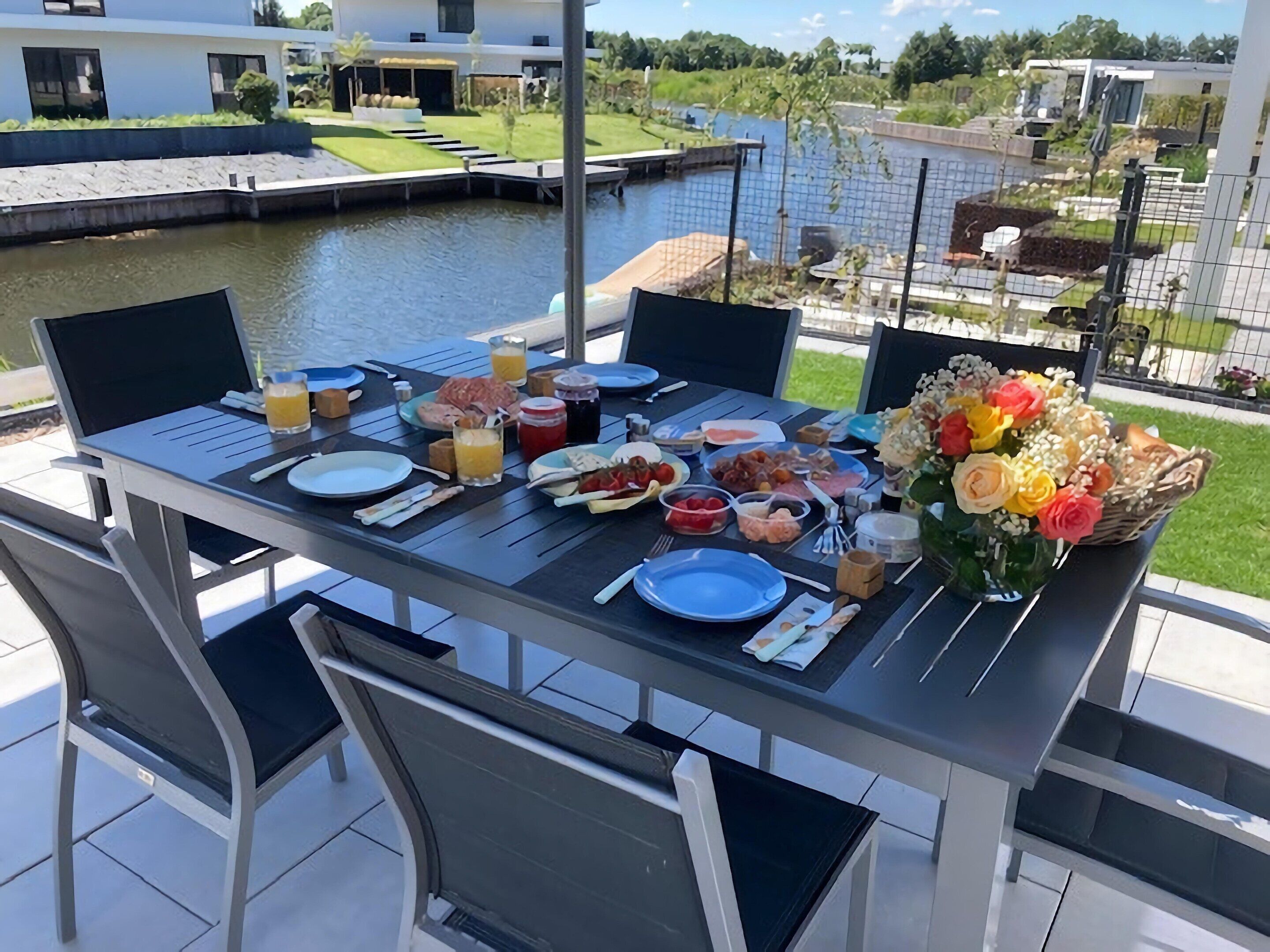 A dining table set outdoors with various dishes, a laptop, and a bouquet of flowers.
