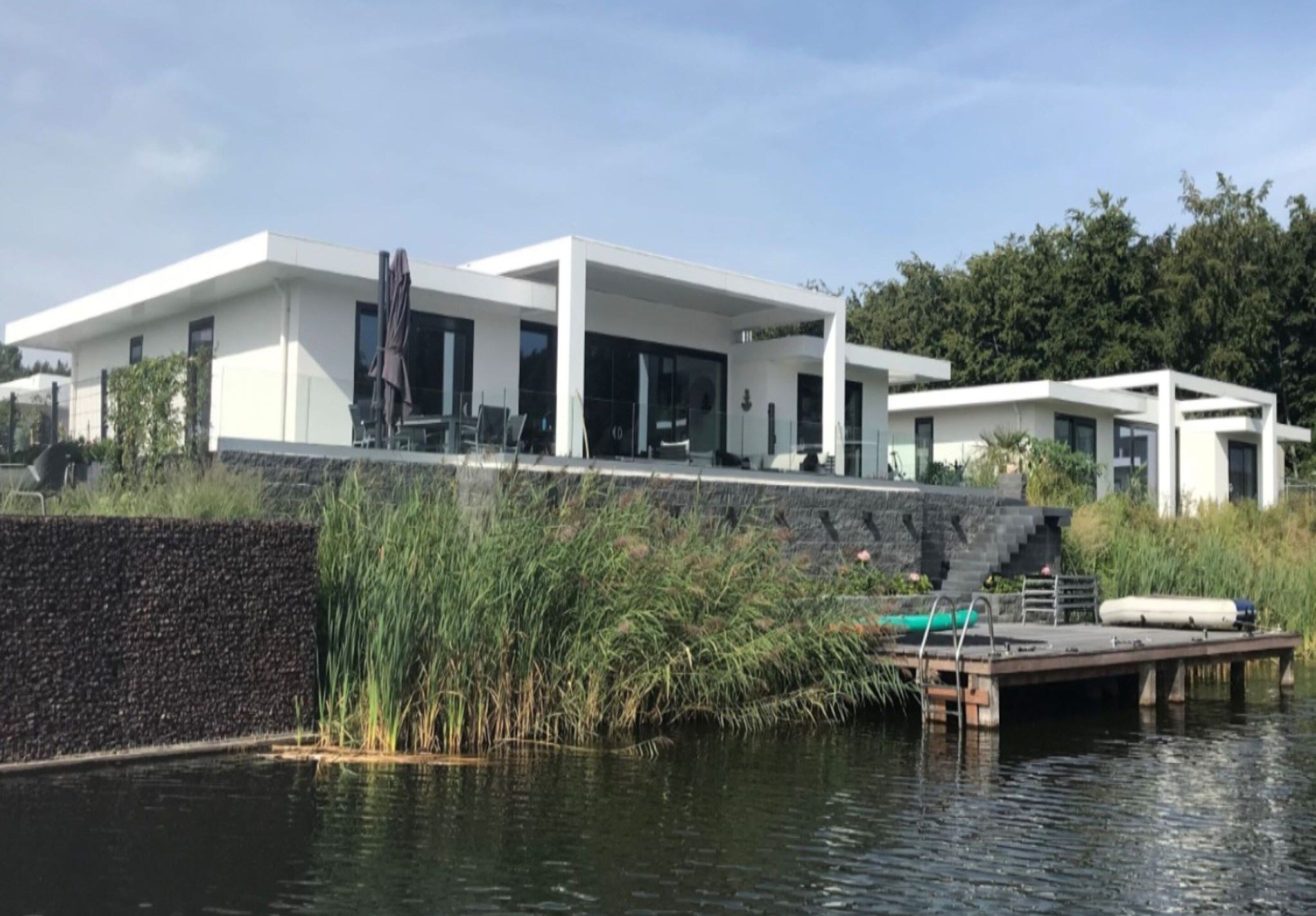 Une maison moderne dotée d’une grande façade vitrée, d’un quai et d’un étang.