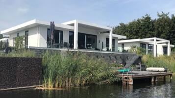 A modern house with a large glass facade, a dock, and a pond.