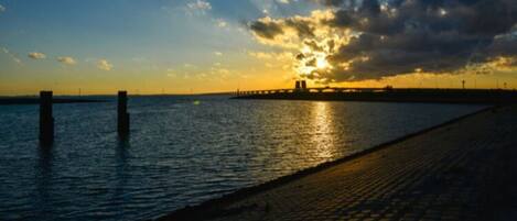 A sunset over a calm body of water with a paved walkway and a distant pier.