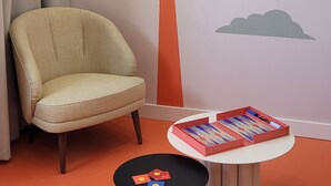 A room with a beige armchair, a small round table with a book, and a wall mural of a tree and clouds. - SEAKUB HOTEL (Royan)