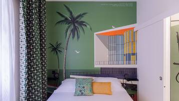 A bedroom with a bed, a green wall mural, a window with orange and blue panels, and a white door.