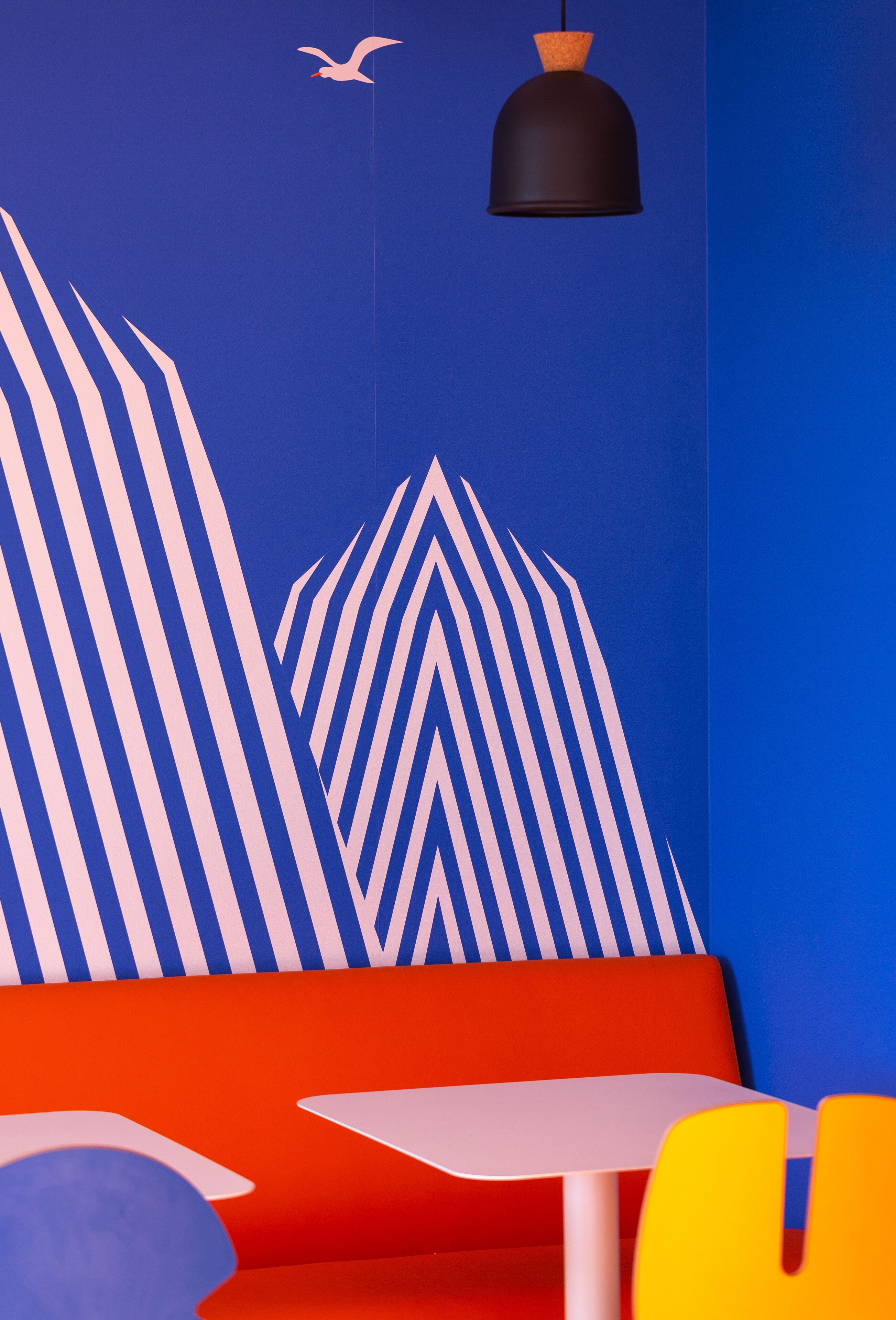 A vibrant interior with a blue and red color scheme, featuring a table and chairs, a hanging light fixture, and abstract wall art.