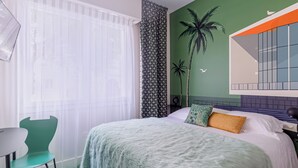 A modern bedroom with a bed, a chair, a table, and a green wall with a palm tree mural. - SEAKUB HOTEL (Royan)