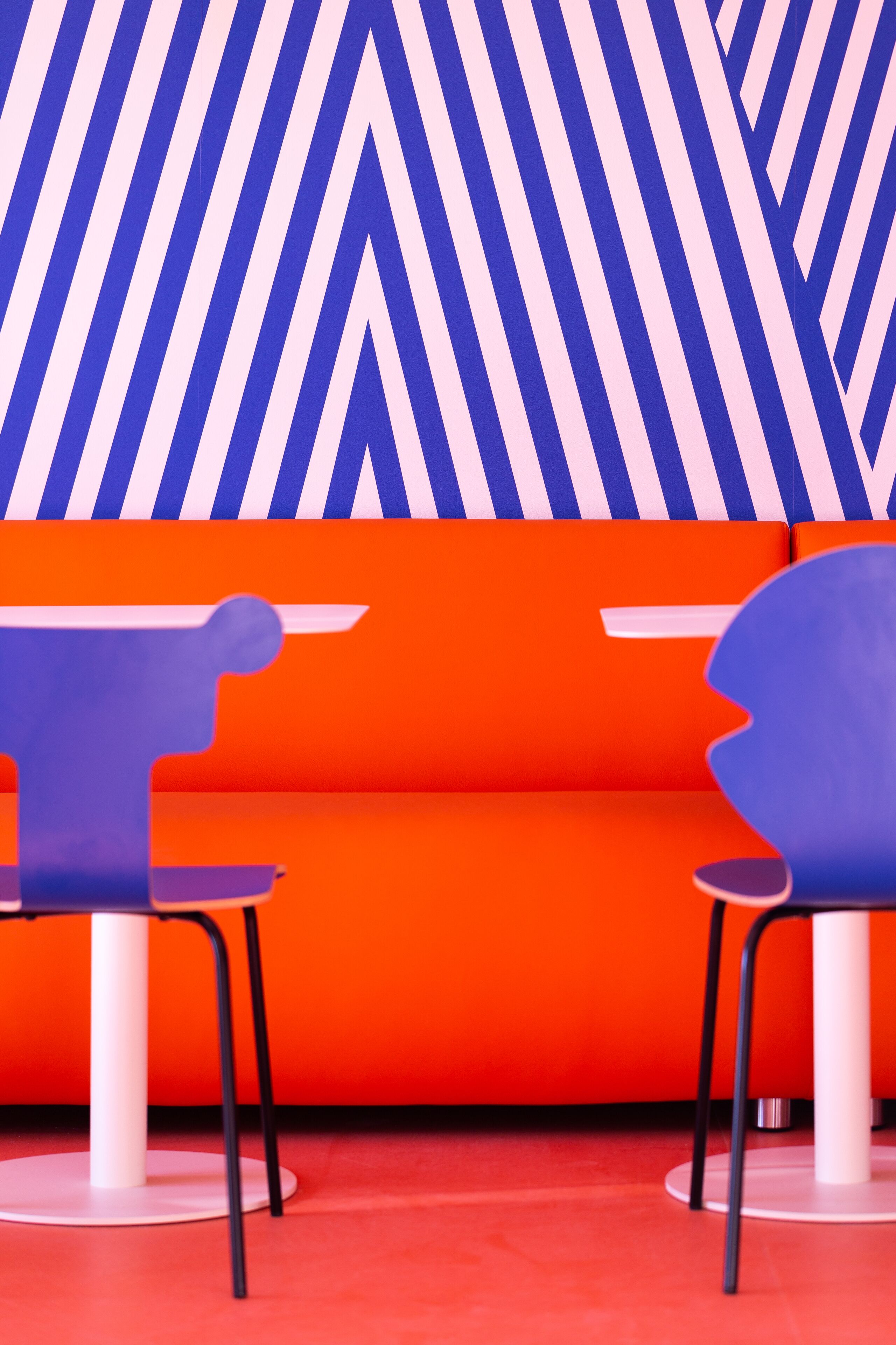 A vibrant interior with a chevron-patterned wall, a red sofa, and two uniquely designed purple chairs.