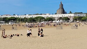A beach with people sunbathing and playing volleyball, a large building in the background, and a clear blue sky. - SEAKUB HOTEL (Royan)