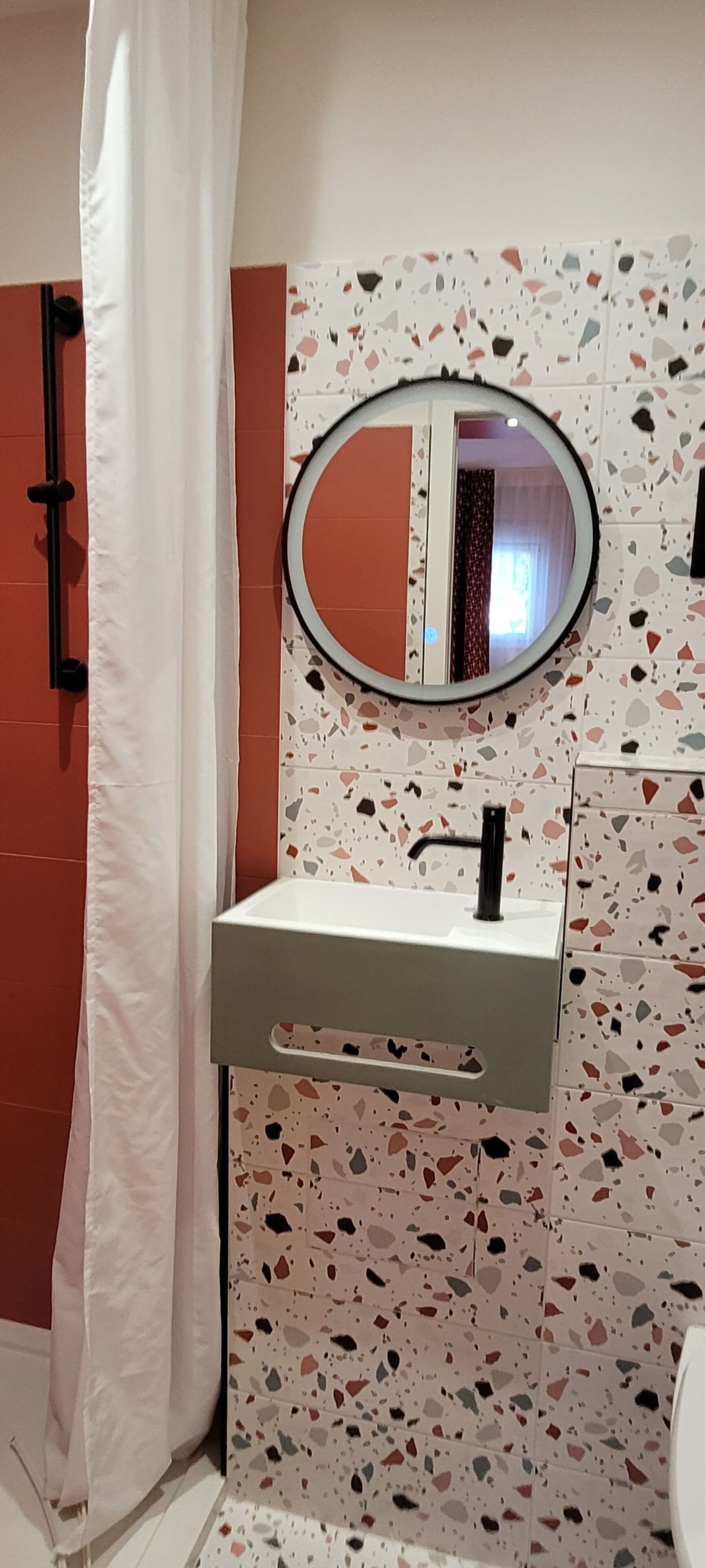 A bathroom with a white sink, a round mirror, and a shower curtain. The walls have a terrazzo tile pattern.