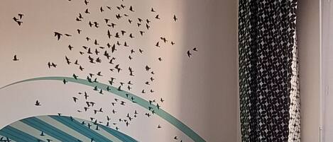 Ein Schlafzimmer mit einem Bett, Kissen, einer Wand mit Vogelaufkleber und einem Vorhang.