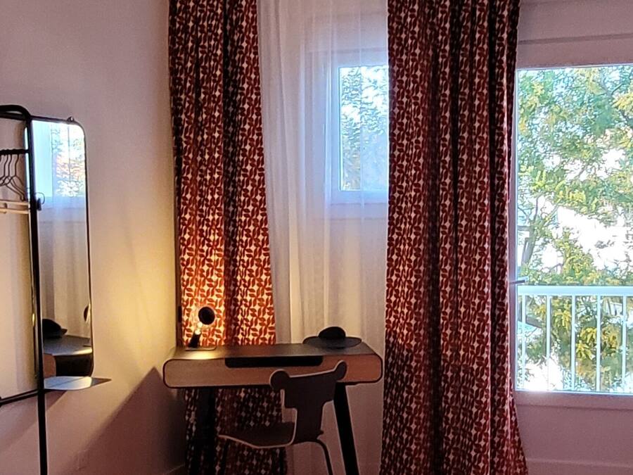 A bedroom with a large bed, a desk, and a chair. There is a window with curtains and a view of trees outside.