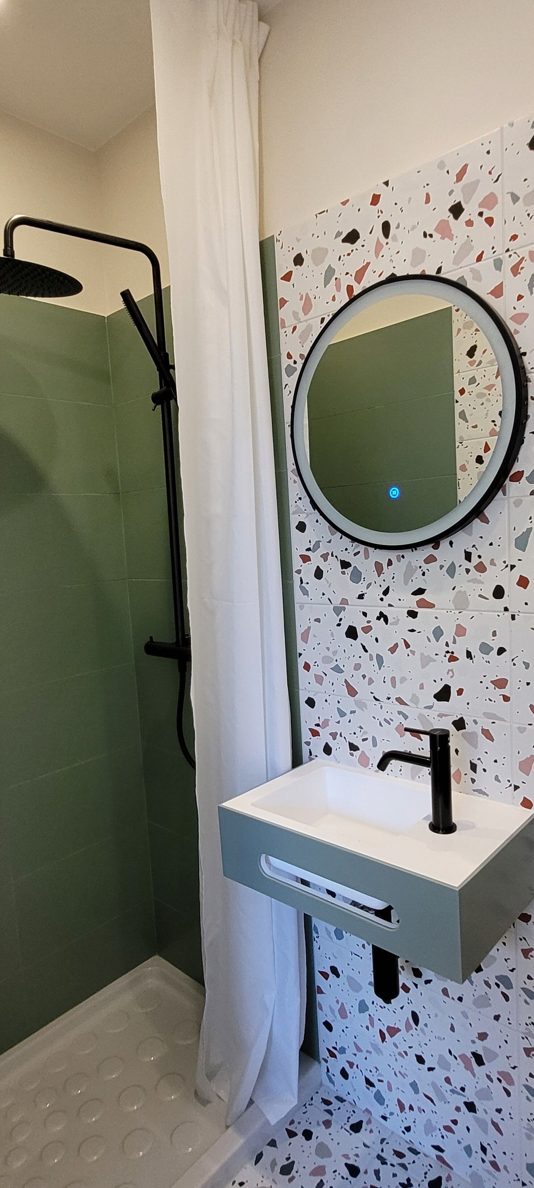 A bathroom with a shower, a sink with a mirror, and a terrazzo tile wall.