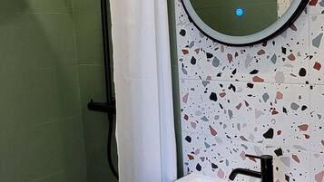 A bathroom with a shower, a sink with a mirror, and a terrazzo tile wall.