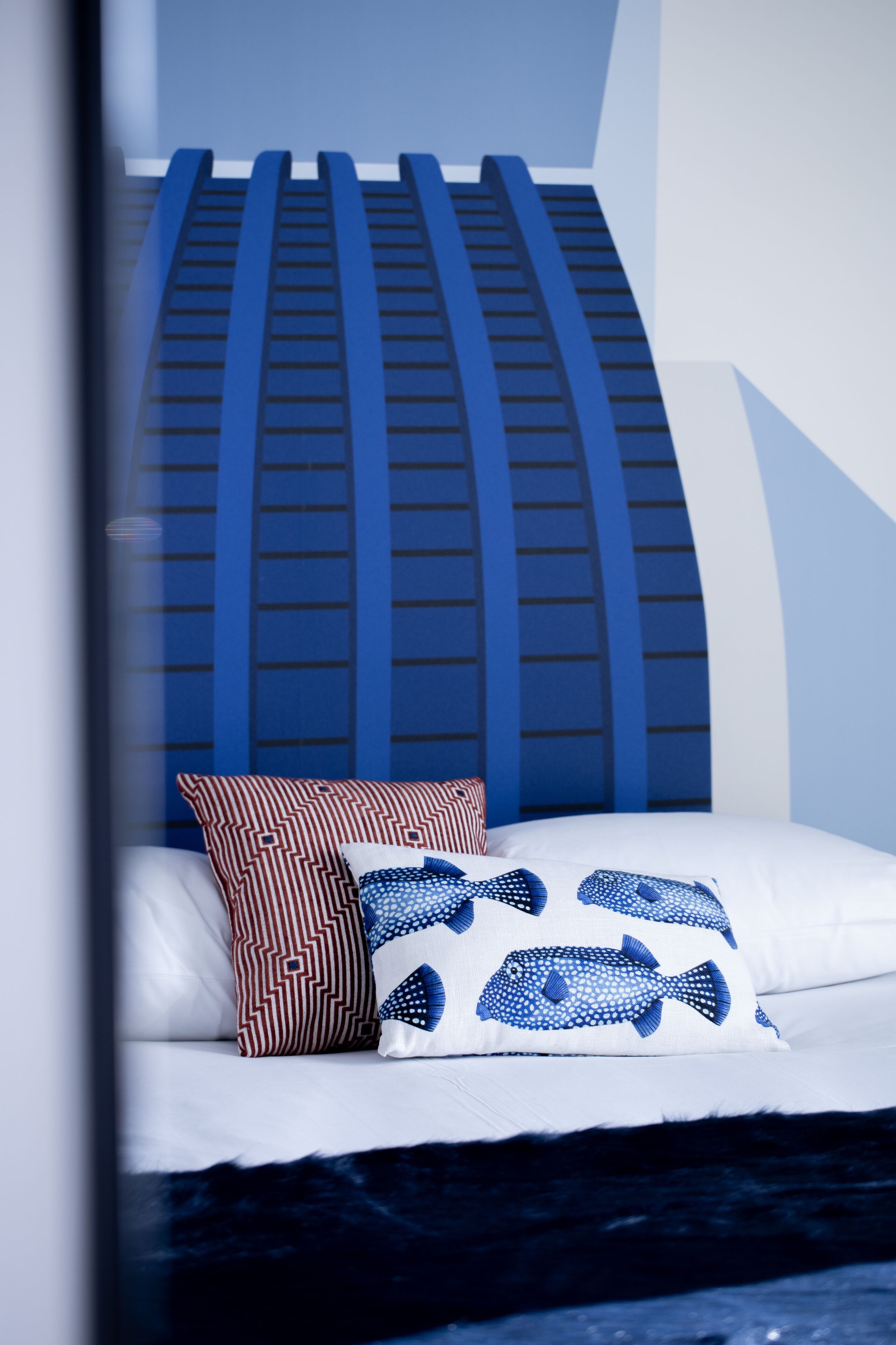Ein Bett mit weißer Matratze, Kissen in blau-weißem Muster und einem blauen Kopfteil mit vertikalen Linien.