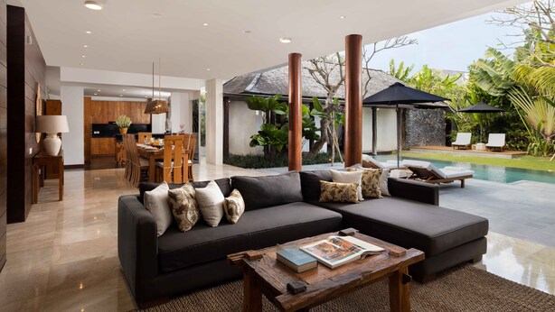 A modern living room with a sectional sofa, a coffee table, and a dining area in the background.