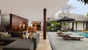 A modern living area with a sofa, dining table, and chairs, a poolside lounge area, and a staircase.