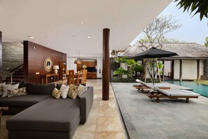 A modern living room with a sectional sofa, a dining area, and a poolside lounge.