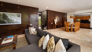 A modern living room with a dark sofa, a wooden coffee table, and a dining area with a wooden table and chairs.