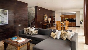 A modern living room with a dark wood accent wall, a sectional sofa, a wooden coffee table, and a dining area in the background.