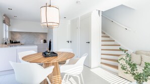 A modern kitchen with white cabinetry, a wooden dining table with white chairs, and a staircase leading to a living area with a sofa and a plant. - Farmhouse in Zeeland With Saltwater Pool (Oostkapelle)