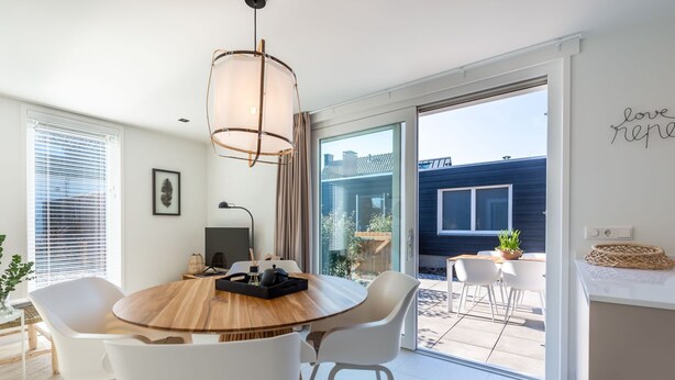 A modern dining area with a wooden table, white chairs, and a pendant light. - Farmhouse in Zeeland With Saltwater Pool (Oostkapelle)