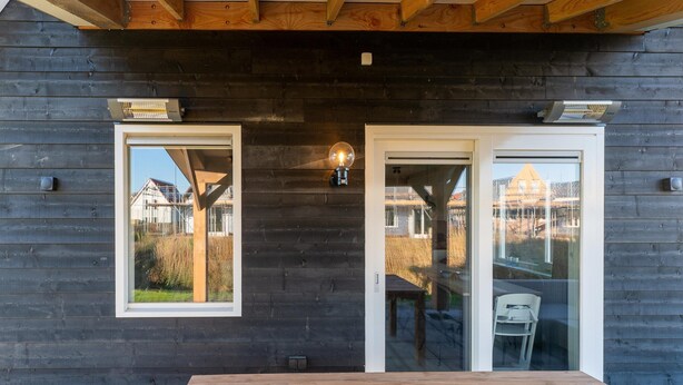 A wooden exterior with a glass door and windows, a wooden table, and a light fixture. - House Near Scherpenisse Beach With Garden (Scherpenisse)