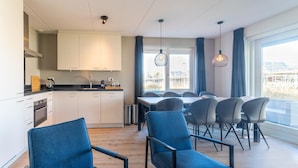 A modern kitchen with white cabinets, a dining area with blue chairs, and large windows offering a view of the outside. - House Near Scherpenisse Beach With Garden (Scherpenisse)