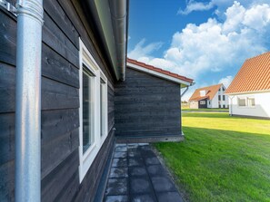 A residential building with a dark wooden exterior, a visible window, and a paved pathway leading to a grassy area. - House Near Scherpenisse Beach With Garden (Scherpenisse)