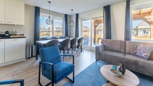 A modern living room with a sofa, a dining table with chairs, a kitchen area, and large windows offering views of the outside. - House Near Scherpenisse Beach With Garden (Scherpenisse)