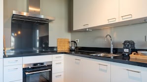 A modern kitchen with white cabinets, stainless steel appliances, and a black countertop. - House Near Scherpenisse Beach With Garden (Scherpenisse)