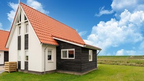 A two-story house with a red-tiled roof, white and black exterior walls, and a grassy landscape in the background. - Holiday Home in Zeeland Near Nature Reserve (Scherpenisse)