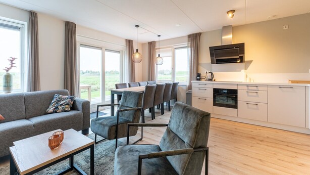 A modern living room with a sofa, chairs, and a dining area. There is a kitchen with a microwave and cabinets. - Holiday Home in Zeeland Near Nature Reserve (Scherpenisse)