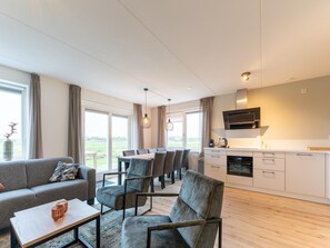 Un salon moderne comprenant un canapé, des fauteuils et un coin repas. On y trouve également une cuisine équipée d’un four à micro-ondes et de placards.