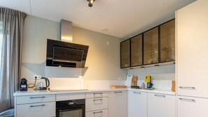 A modern kitchen with white cabinetry, a built-in oven, a stove, and a microwave. There is a glass cabinet above the countertop, and a window with curtains on the left. - Holiday Home in Zeeland Near Nature Reserve (Scherpenisse)