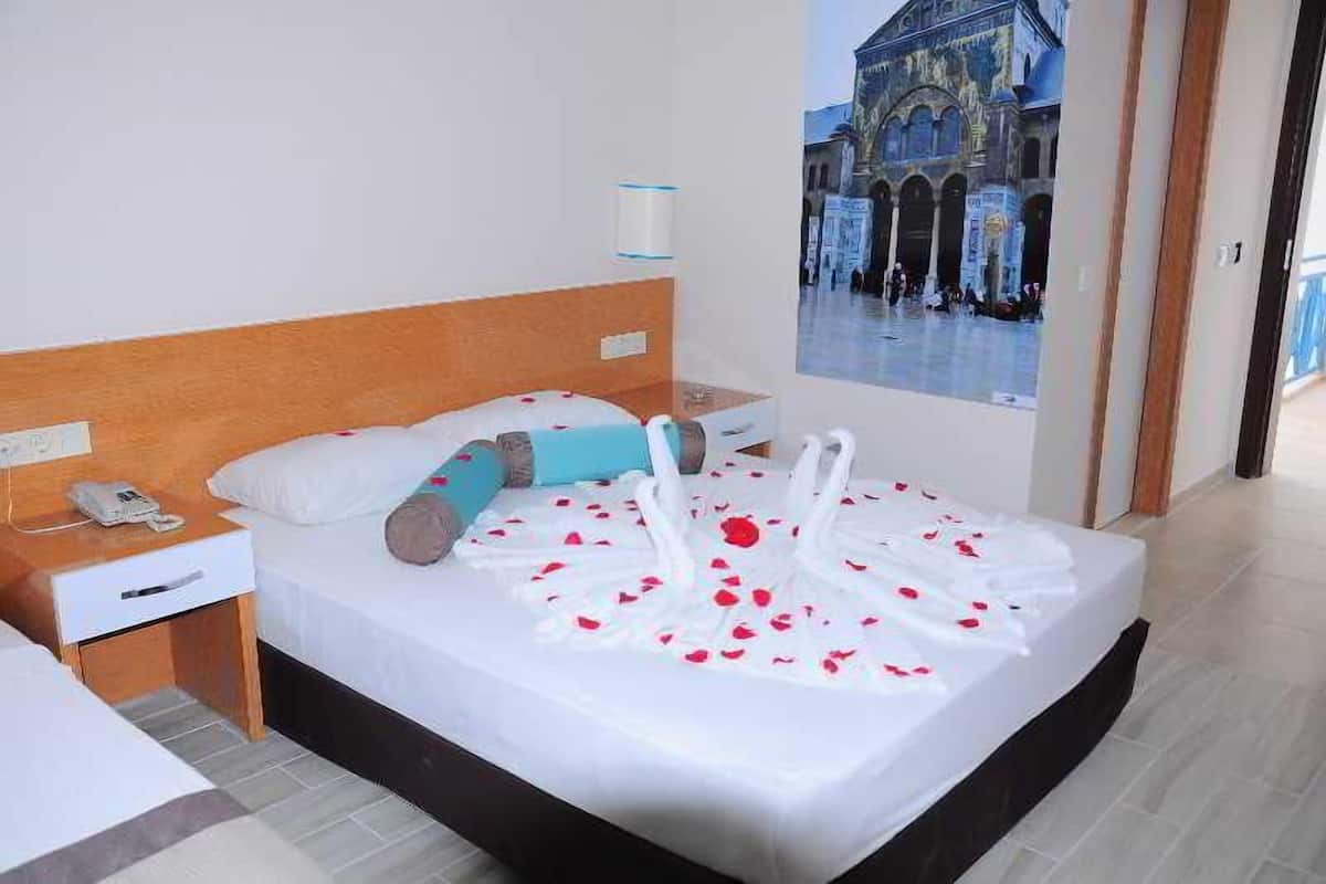 Una habitación de hotel con una cama decorada con pétalos de rosa y cisnes, una mesita de noche con un teléfono, y un cartel de un edificio histórico.