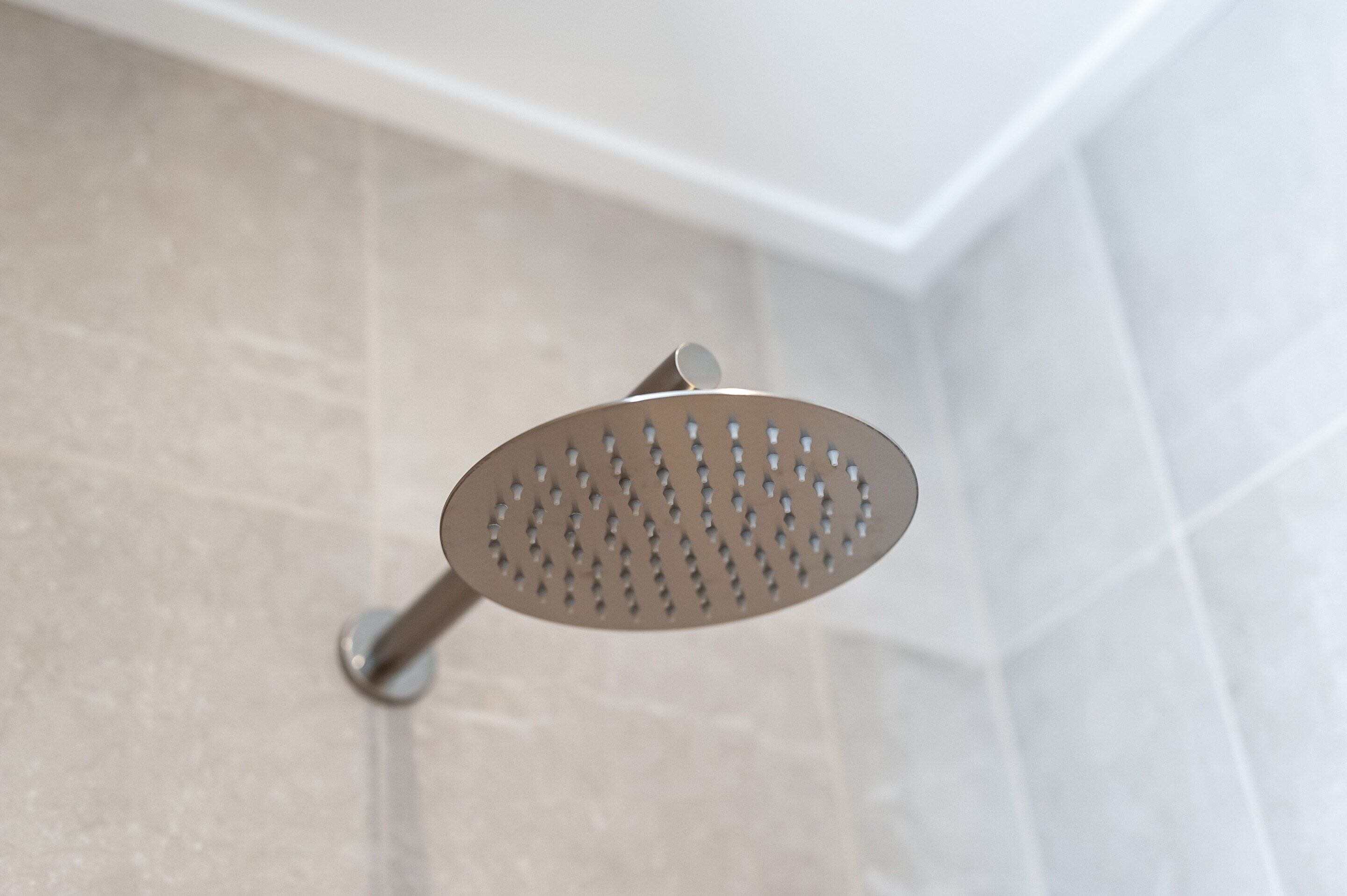 Um chuveiro com design perfurado, fixado numa parede revestida com azulejos.