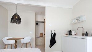A modern, minimalist bedroom with a bed, a small table, and chairs. Adjacent is a compact kitchen with a sink, a kettle, and a coffee machine. - Holiday Home in Oostkapelle Near the Beach (Oostkapelle)