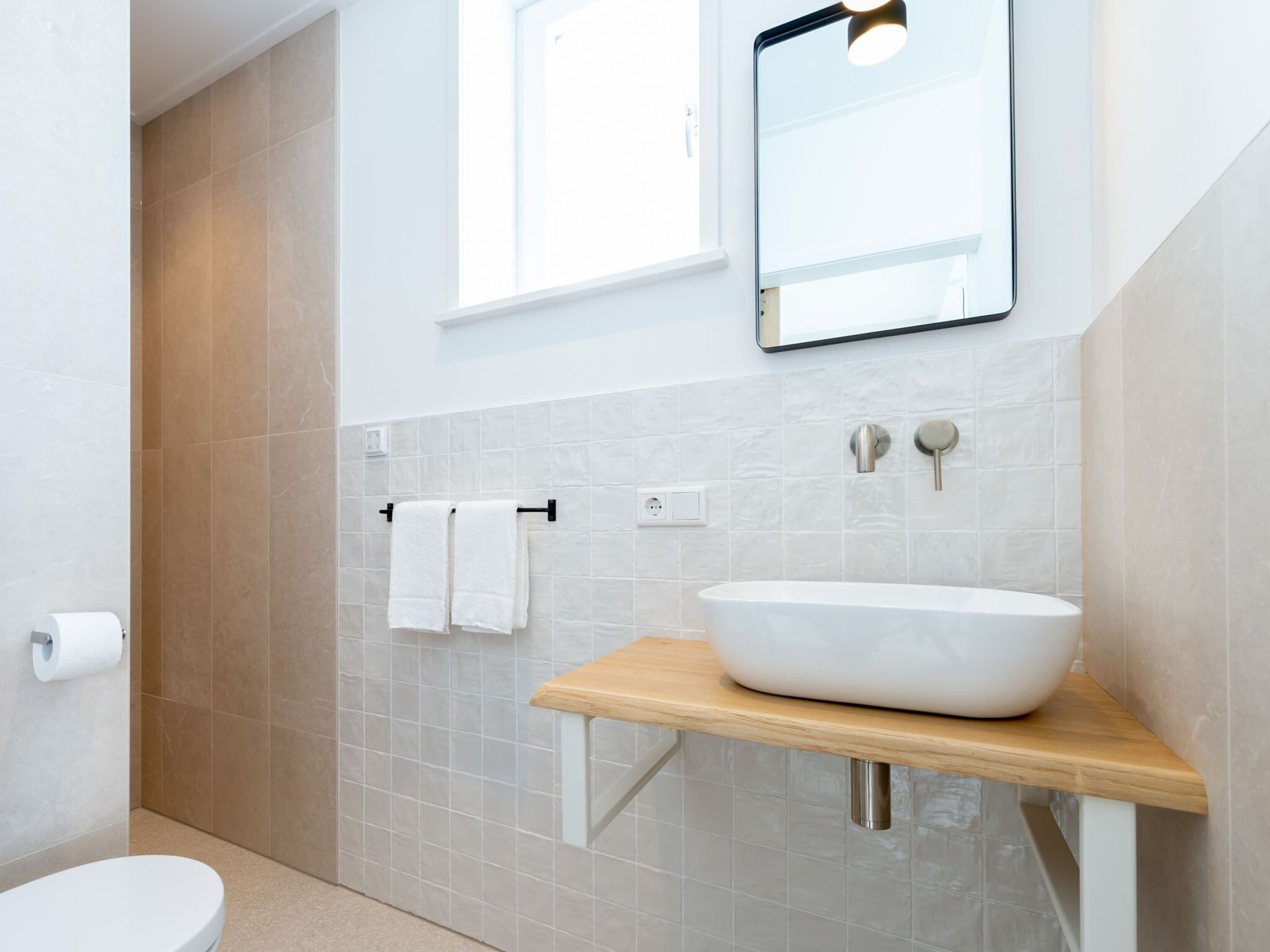 A modern bathroom with a white sink on a wooden shelf, a towel rack with two white towels, and a mirror above the sink.